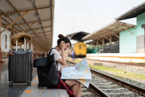 Молодая женщина путешественник с рюкзаком ищет карту в ожидании поезда, азиатский турист на железнодорожной платформе на вокзале. Концепция отпуска, путешествия, путешествия и летнего путешествия — стоковое фото