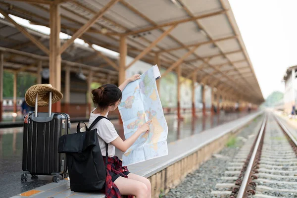 Mujer asiática joven utilizando el mapa local genérico, situado solo en la plataforma de la estación de tren con el equipaje. Vacaciones de verano viajando o joven mochila turística viajero concepto — Foto de Stock