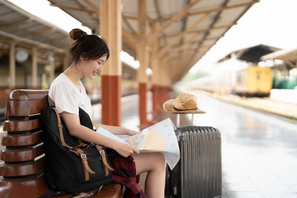 Joven mujer asiática viajero sentado con mapa elegir dónde viajar y bolsa de espera para tren en la estación de tren, vacaciones de verano concepto de viaje — Foto de Stock