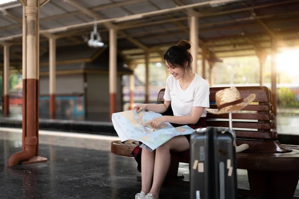 Szczęśliwy młody azjatycki kobieta podróżnik lub Backpacker za pomocą mapy wybrać, gdzie podróżować z bagażem na dworcu kolejowym, letnia koncepcja podróży wakacje — Zdjęcie stockowe