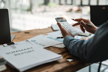 Accountant or bookkeeper working with calculator to calculate business data summary report, accountancy document and laptop computer at office, business concept