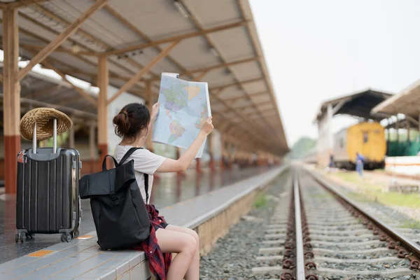一般的なローカルマップを使用して若いアジアの女性は、単独で荷物を駅のプラットフォームに座っている。夏休み旅行や若い観光バックパック旅行のコンセプト — ストック写真