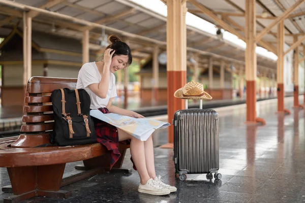 Joven mujer asiática viajero sentado con mapa elegir dónde viajar y bolsa de espera para tren en la estación de tren, vacaciones de verano concepto de viaje — Foto de Stock