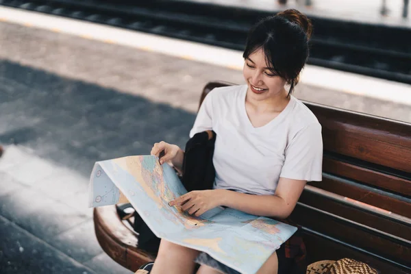 Feliz joven mujer asiática viajero o mochilero usando mapa elegir dónde viajar con el equipaje en la estación de tren, vacaciones de verano concepto de viaje — Foto de Stock