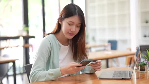 微笑的年轻女性顾客在家里拿着信用卡和智能手机。快乐的女性购物者在网上商店里使用即时方便的移动支付购买。电子银行应用软件服务 — 图库视频影像