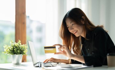 Kredi kartı tutan ve online alışveriş için dizüstü bilgisayar kullanan mutlu bir kadın. Çevrimiçi ödeme alışveriş kavramı