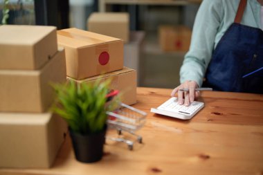 Close up woman start up small business owner calculation at workplace. small business entrepreneur SME or freelance asian woman working with box at home.