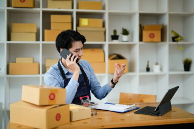 Portre Asyalı adam cep telefonuyla emir alıyor. Küçük işletme girişimcisi KME evde kutu ile çalışıyor, KOBİ dijital teknoloji kavramı.