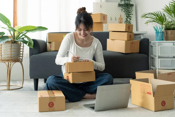 Genç ve çekici Asyalı kadın sahibi girişim işine bakın. Kameraya mutlu bir şekilde bakın. Kutu evde. Paket teslimatını sme tedarik zinciri, tedarik, omnichannel veya koronavirüs karantina konseptinde hazırlayın.