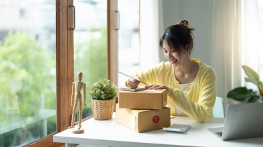 Genç kadın bağımsız çalışma ve denetim listesi ve karton siparişle yazma yatağa evde - KOBİ iş online ve teslimat kavramı kutu