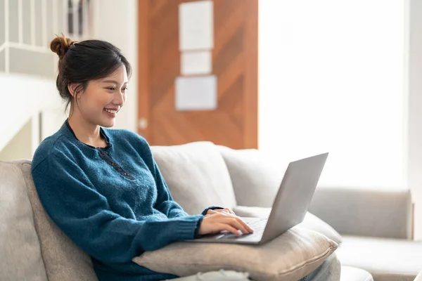 Sorrindo jovem asiático mulher usando laptop, sentado no sofá em casa — Fotografia de Stock