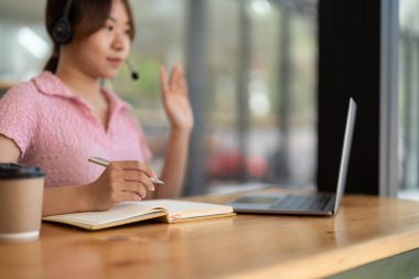 Genç Asyalı kadın evde internet ağları dinlerken, kulaklık takarken, bilgisayar kullanırken, yabancı dil öğrenirken, e-öğrenirken not alıyor, karantina sırasında evde kalıyor.