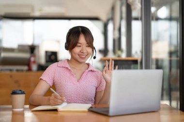 Genç Asyalı kadın evde internet ağları dinlerken, kulaklık takarken, bilgisayar kullanırken, yabancı dil öğrenirken, e-öğrenirken not alıyor, karantina sırasında evde kalıyor.