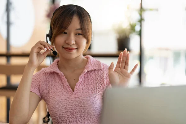 미소짓는 여학생은 무선 헤드폰으로 선생님 과 온라인으로 공부하고, 행복 한 젊은 아시아인 여성은 언어를 배우고, — 스톡 사진