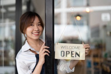Önlüklü güzel Asyalı genç barista kadın elinde tabletle kafenin önünde açık tabela panosuyla dikiliyor. İş sahibi başlangıç konsepti