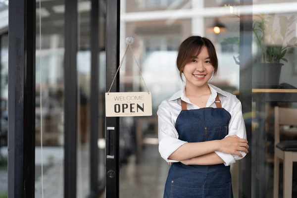 Linda asiática jovem barista mulher no avental segurando tablet e de pé na frente da porta do café com placa de sinal aberto. Conceito de startup proprietário de empresa — Fotografia de Stock