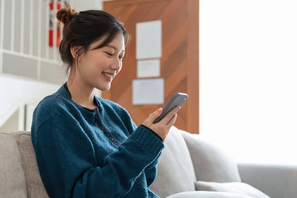 Mulher sorrindo atraente usando telefone inteligente enquanto sentado no sofá em casa. Conceito de comunicação e aconchego — Fotografia de Stock