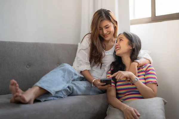 Dos jóvenes felices mujeres asiáticas casuales que se divierten con el teléfono inteligente en casa. Lesbianas millennial pareja concepto. —  Fotos de Stock