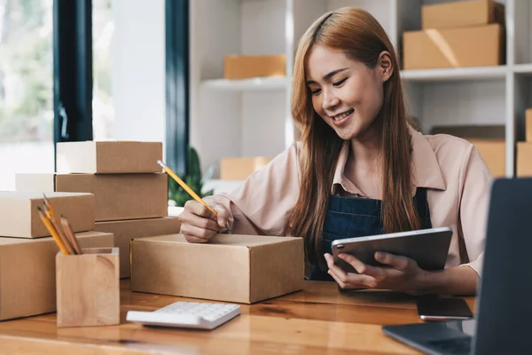 Happy young start up small business owner packing writing address on cardboard box. freelance woman seller prepare parcel box of product for deliver to customer. Online selling, shipping concept.