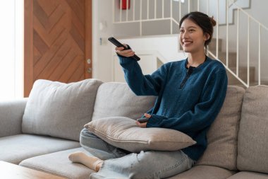 Mutlu ev oturma odası Asyalı kadın TV izliyor apartman dairesindeki kanepede dinleniyor..
