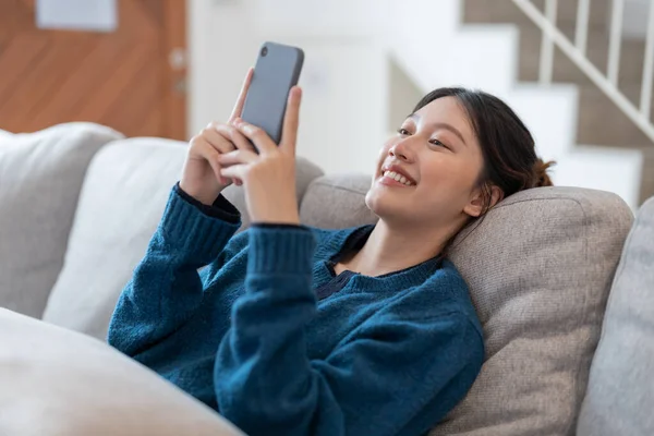 Glückliche Junge Asiatin Liegt Auf Sofa Wohnzimmer Und Benutzt Handy — Stockfoto