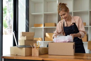 Asyalı kadın çevrimiçi mağaza sahibi küçük işletme sahibi girişimci posta kutusunu paketliyor ve teslimat paketini masaya hazırlıyor. Ticaret düşüş nakliye hizmeti konsepti