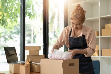 Asyalı kadın çevrimiçi mağaza sahibi küçük işletme sahibi girişimci posta kutusunu paketliyor ve teslimat paketini masaya hazırlıyor. Ticaret düşüş nakliye hizmeti konsepti