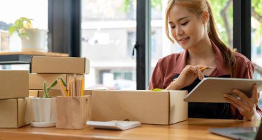 Asyalı kadın girişimci elinde kalemle hesap makinesi, ev ofisinin mali giderlerini hesaplıyor, çevrimiçi pazar paketleme kutusu teslimatı, girişimde başarılı küçük işletme sahibi KME, konsept