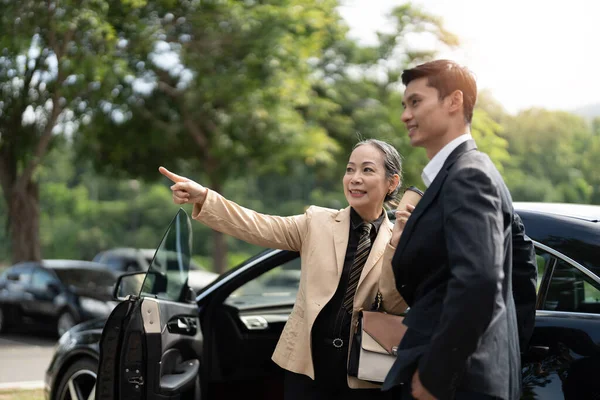 車の公園で若いアジア系男性の同僚と新しいプロジェクトについて話す幸せな高齢のアジアのビジネスマンの女性の議論 — ストック写真