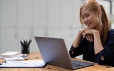 Mutlu Asyalı kadın elleri hesaplamalar yapıyor. Genç bir kadın dizüstü bilgisayara bakıyor, aylık ev giderlerini ve gelirlerini yönetiyor, e-bankacılık başvurusunu kullanıyor, yatırım planlıyor