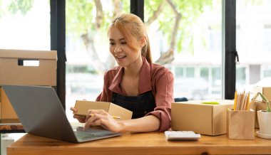 Küçük bir İşletme, KOBİ Sahipleri ve Kadın Girişimciler, KOBİ müşterilerine çevrimiçi iş fikri satmak üzere kutuları paketlemek için hesap makinesiyle çevrimiçi siparişleri kontrol ediyorlar