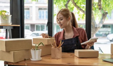 Küçük bir İşletme, KOBİ Sahipleri ve Kadın Girişimciler, KOBİ müşterilerine çevrimiçi iş fikirleri satmak üzere kutu paketlemek için hesap makinesiyle çevrimiçi siparişleri kontrol ediyorlar.