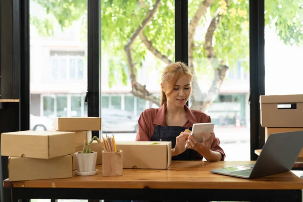 Küçük bir İşletme, KOBİ Sahipleri ve Kadın Girişimciler, KOBİ müşterilerine çevrimiçi iş fikri satmak üzere kutuları paketlemek için hesap makinesiyle çevrimiçi siparişleri kontrol ediyorlar