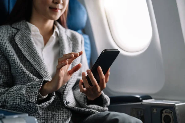 Travel and technology. Young woman in plane using smartphone while sitting in airplane seat.