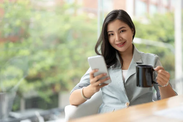 Smiling asian businesswoman using phone in office. Small business entrepreneur looking at her mobile phone and smiling
