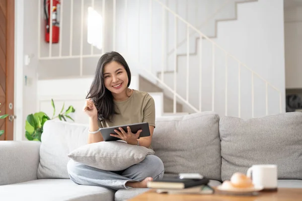 Schöne Attraktive Junge Asiatin Sitzt Auf Grauem Sofa Und Benutzt — Stockfoto