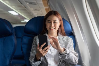 Çekici Asyalı kadın uçakta cep telefonu kullanıyor, kameraya bakıyor.