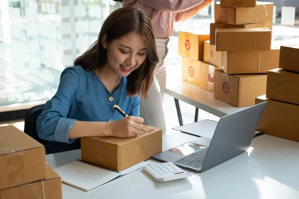 Asian business woman on sofa using a laptop computer checking customer order online shipping boxes at home. Starting SME Small business entrepreneur freelance. Online business, SME Work home concept.