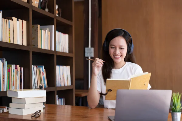 幸せなアジアの女性は コンピュータ上の自宅の書き込み研究で机に座っている 若い混合レースの女性の笑顔は ラップトップ上で遠くの仕事は Web上でコースを取る 学習の概念 — ストック写真
