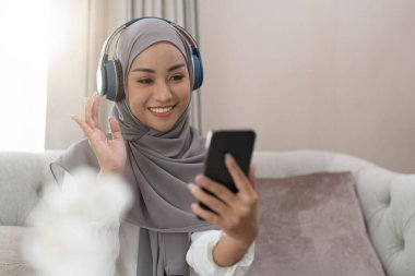 Kanepede oturan Müslüman kadın ve cep telefonundan arayan video konferansı. Müslüman Asyalı kadın video çağrısı