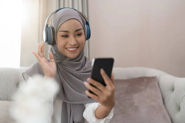 穆斯林妇女坐在沙发上 开电视电话会议 打电话给手机 穆斯林亚洲妇女视频通话 — 图库照片