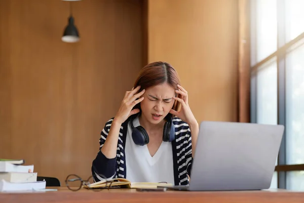 Stressed Asian woman cover her face with hand and feel upset from work in front of laptop computer on desk at office,Stress office lifestyle concept