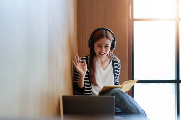 Asian tutor of language start online lesson with trainee wave hand smiling looks at pc screen. A woman in headphones communicating distantly, e-learning process, application usage concept