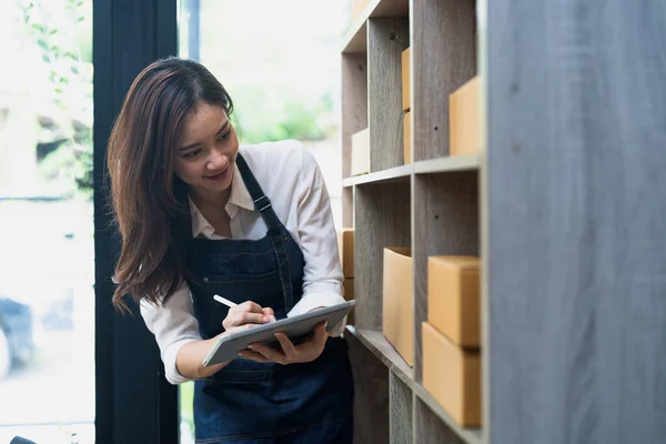 Asian female entrepreneur checking orders to arrange the produce before packing the products in the inner boxes with the customers. Freelance concepts.