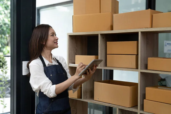 Asian female entrepreneur checking orders to arrange the produce before packing the products in the inner boxes with the customers. Freelance concepts.