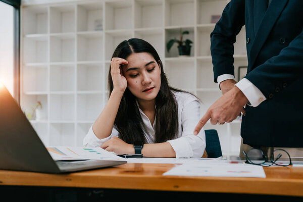 Furious boss scolding young frustrated interns. Ineffective office workers sitting at the table and listening to irritated boss yelling with bored and annoyed expressions.