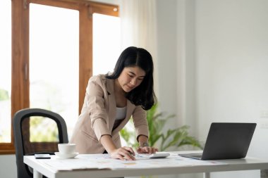 Woman with paperwork using calculator and laptop computer working at home office.