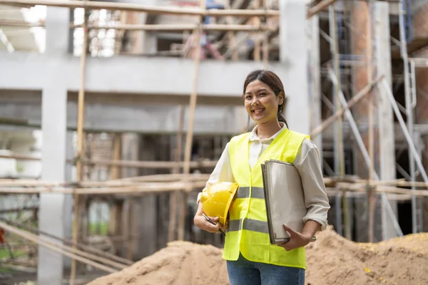 Portrait of asian female site contractor engineer with hard hat holding blue print paper.