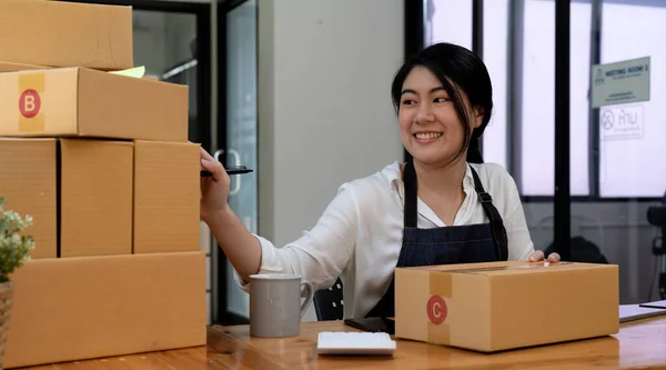 Smiling entrepreneur checking order on delivery box on work desk at home.