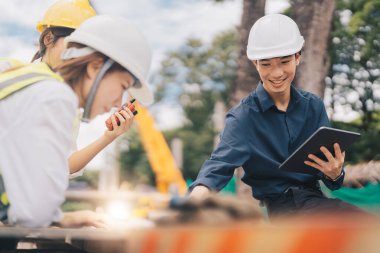 Young asian architects and engineer discussing blueprints at construction site.